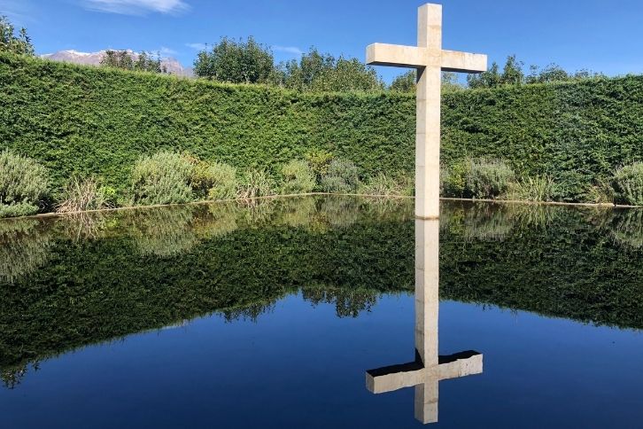 Cross in a pool with its reflection mirrored in the water, a green wall surrounding the water